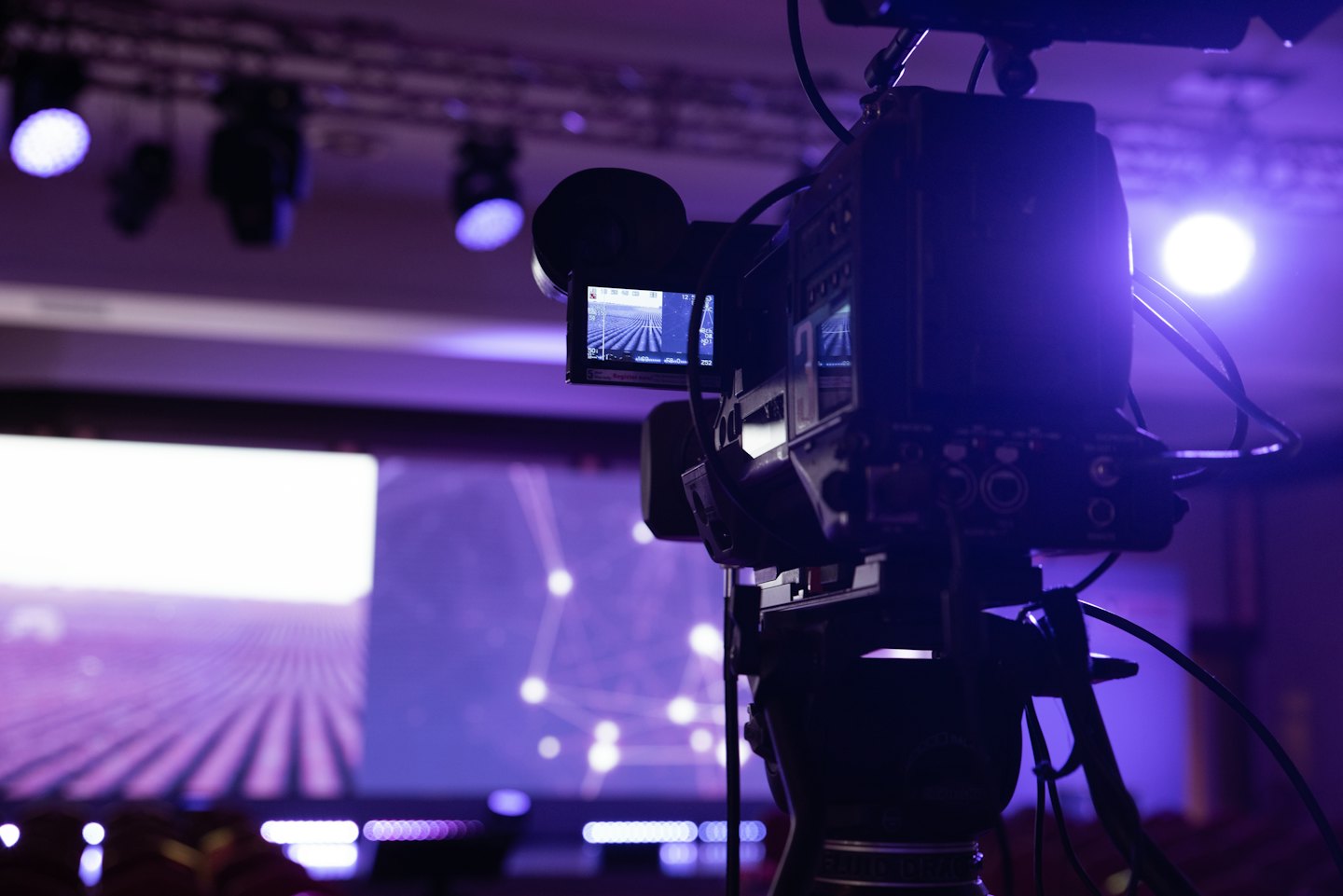 Professional video camera on a tripod recording a conference presentation.